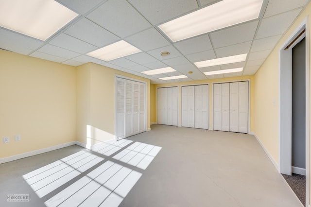 unfurnished bedroom featuring a drop ceiling and multiple closets