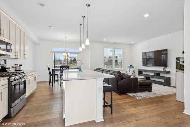 kitchen featuring appliances with stainless steel finishes, a breakfast bar, white cabinetry, hanging light fixtures, and a center island with sink