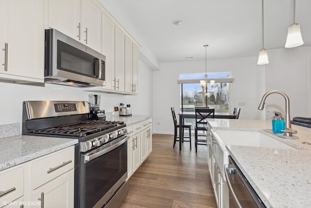 kitchen featuring stainless steel appliances, hanging light fixtures, white cabinets, and light stone counters