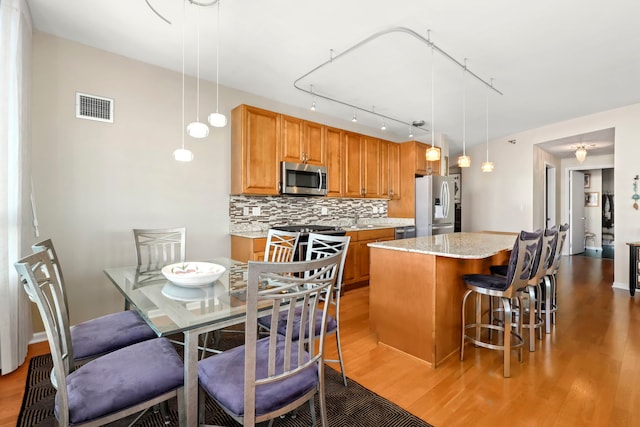 kitchen with stainless steel appliances, a center island, wood-type flooring, decorative backsplash, and decorative light fixtures