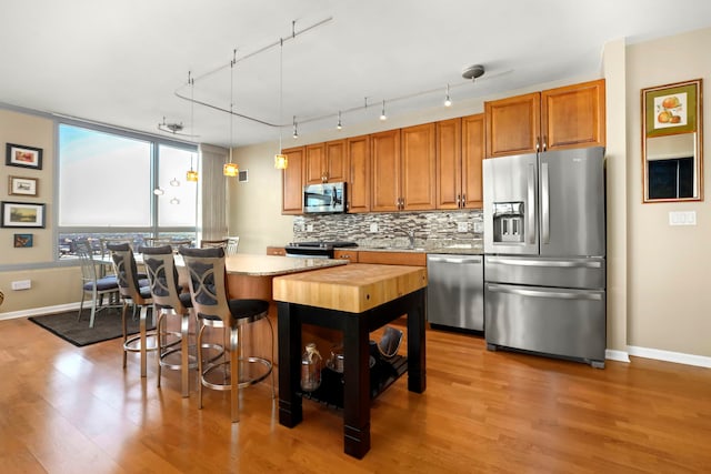 kitchen featuring light hardwood / wood-style flooring, a kitchen island, pendant lighting, stainless steel appliances, and backsplash