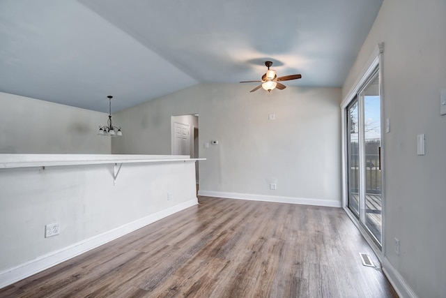 unfurnished living room featuring ceiling fan with notable chandelier, wood-type flooring, and vaulted ceiling