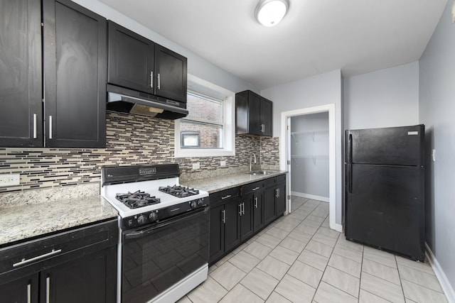 kitchen with sink, white gas stove, black fridge, light stone countertops, and backsplash