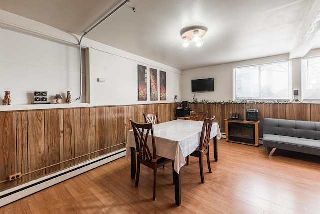 dining space with baseboard heating, wood walls, and hardwood / wood-style flooring