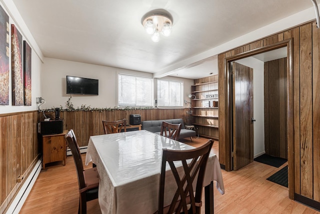 dining area featuring light hardwood / wood-style flooring, wooden walls, and a baseboard radiator