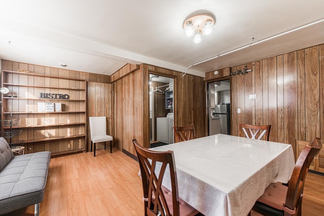 dining room featuring light hardwood / wood-style flooring, wood walls, built in shelves, and washer / clothes dryer