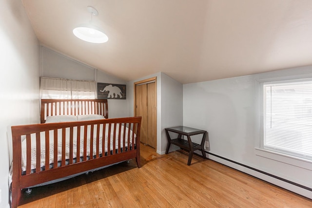 bedroom with a baseboard heating unit, vaulted ceiling, a closet, and hardwood / wood-style floors