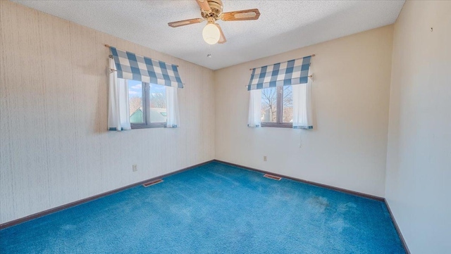 empty room featuring dark carpet, visible vents, plenty of natural light, and a textured ceiling