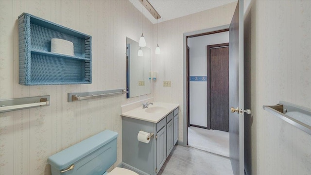 bathroom with toilet, wallpapered walls, and vanity