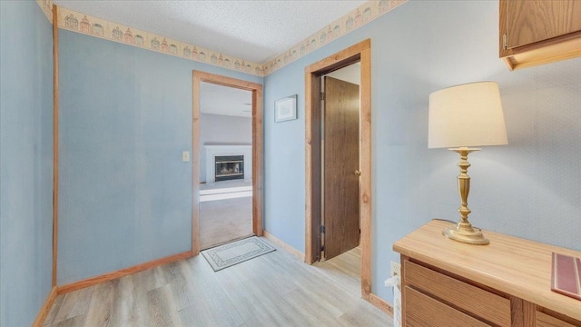 hall featuring baseboards, light wood-style flooring, and a textured ceiling