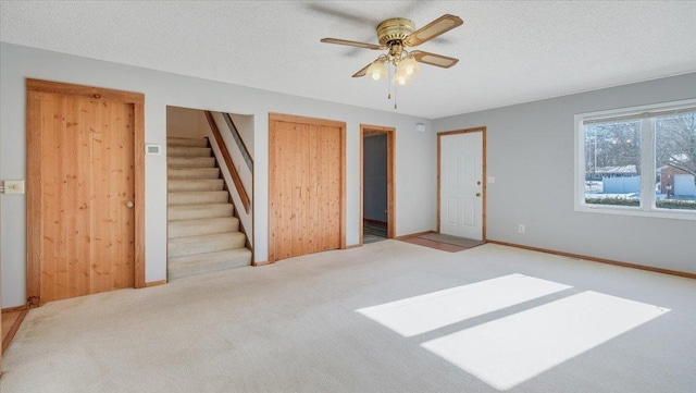 unfurnished bedroom featuring multiple closets, baseboards, a textured ceiling, and light colored carpet