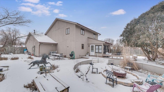 snow covered house with an outdoor fire pit and fence