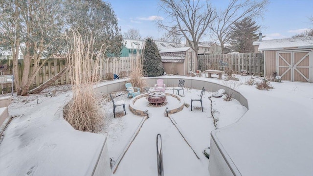 snowy yard with an outdoor fire pit, fence, and a storage shed