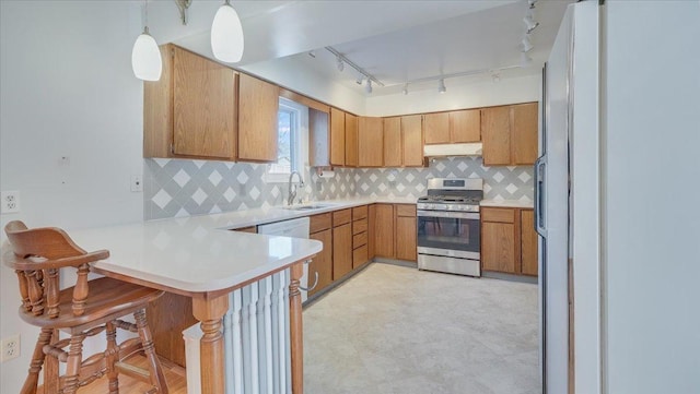 kitchen featuring stainless steel gas range oven, under cabinet range hood, a peninsula, light countertops, and decorative light fixtures