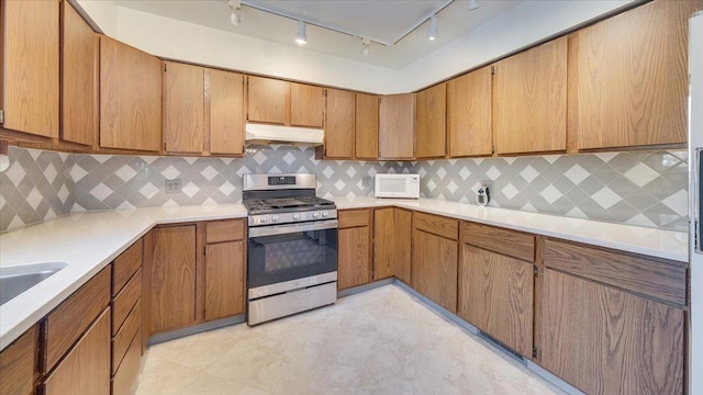 kitchen with brown cabinetry, white microwave, light countertops, under cabinet range hood, and stainless steel range with gas stovetop