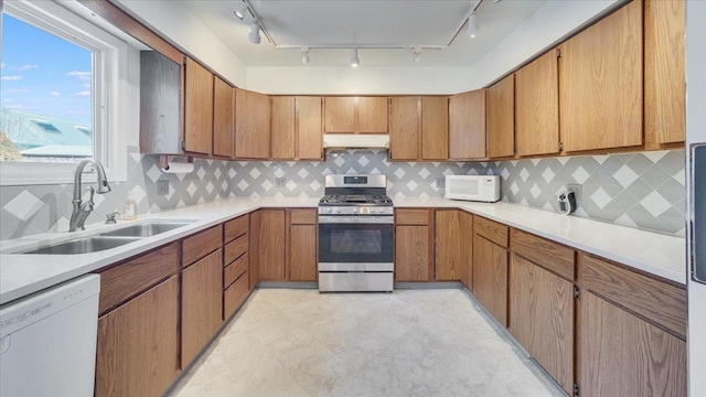 kitchen featuring under cabinet range hood, white appliances, a sink, light countertops, and brown cabinets