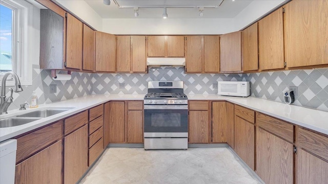 kitchen featuring white appliances, brown cabinetry, light countertops, under cabinet range hood, and a sink