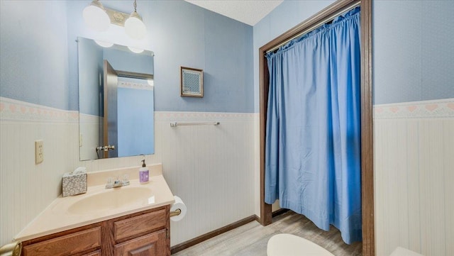 full bath with toilet, a wainscoted wall, wood finished floors, and vanity