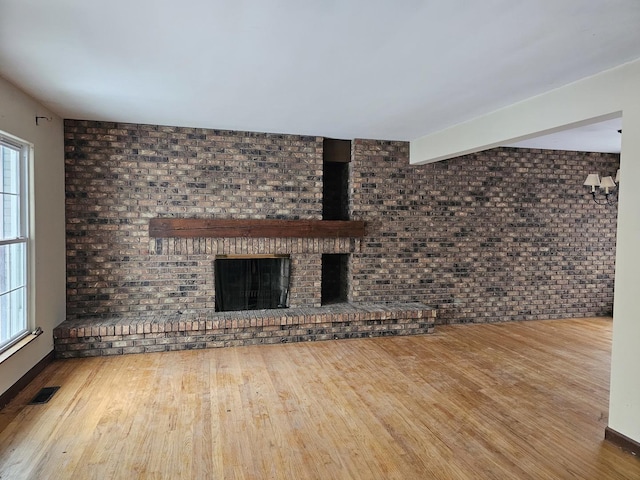 unfurnished living room featuring brick wall, wood-type flooring, and a brick fireplace