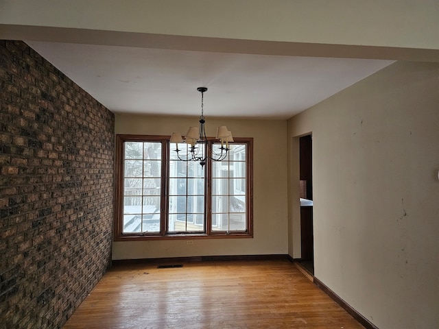 unfurnished dining area with light hardwood / wood-style flooring, a chandelier, and brick wall