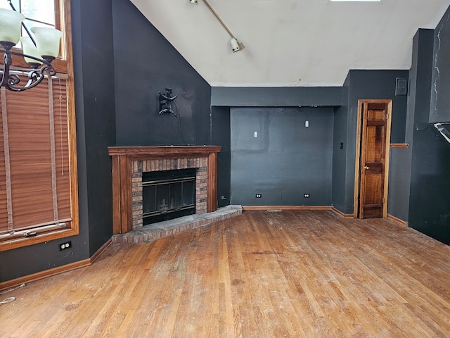 unfurnished living room with a fireplace, light hardwood / wood-style flooring, rail lighting, and vaulted ceiling