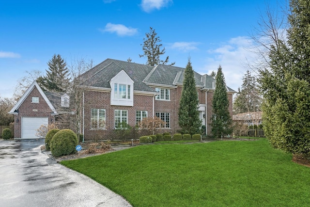 colonial home with a garage, driveway, brick siding, and a front yard