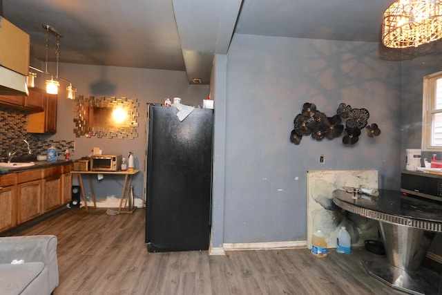 kitchen with pendant lighting, wood-type flooring, sink, backsplash, and black fridge