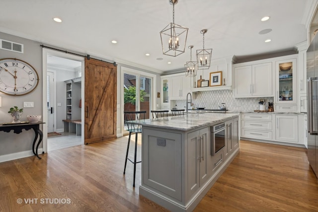 kitchen featuring crown molding, white cabinetry, light stone counters, an island with sink, and a barn door