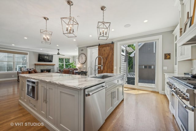 kitchen featuring stainless steel appliances, an island with sink, white cabinets, decorative light fixtures, and a barn door