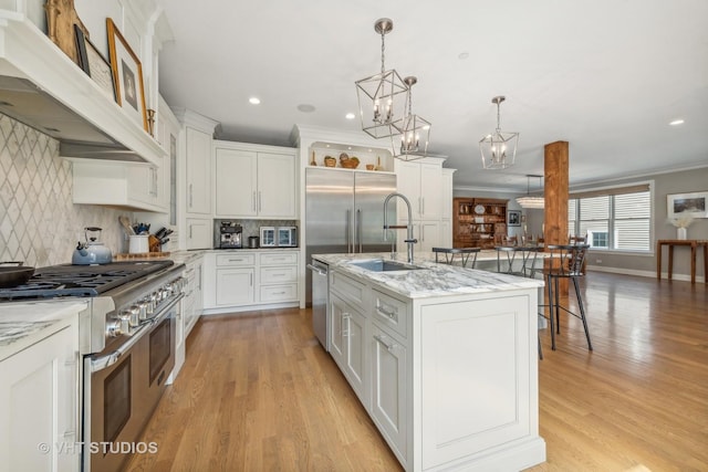 kitchen featuring decorative light fixtures, white cabinets, a kitchen island with sink, light stone counters, and stainless steel appliances