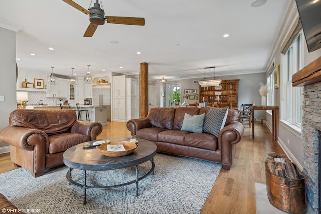 living room featuring a stone fireplace, sink, ceiling fan, light hardwood / wood-style floors, and crown molding