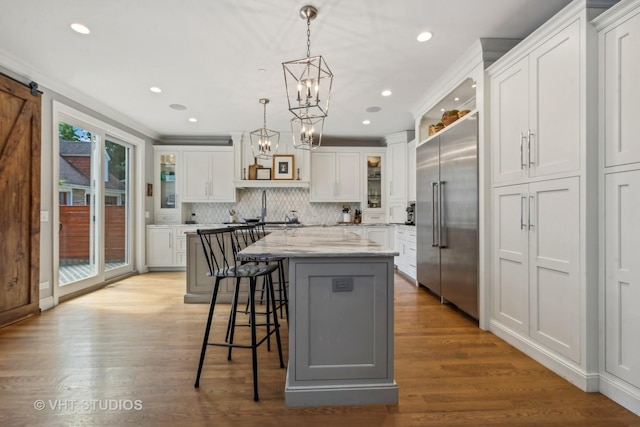 kitchen featuring built in fridge, white cabinets, hanging light fixtures, a center island, and light stone countertops