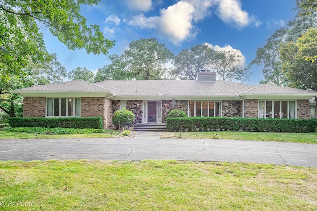 ranch-style home with a front yard, brick siding, and a chimney