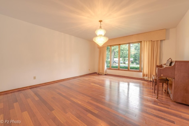 spare room featuring baseboards, wood-type flooring, and an inviting chandelier