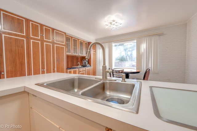 kitchen with brown cabinets, glass insert cabinets, light countertops, and a sink