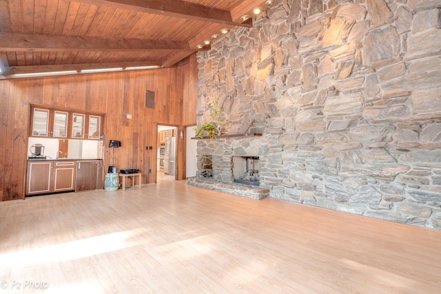 unfurnished living room featuring lofted ceiling with beams, wooden ceiling, wooden walls, a fireplace, and wood finished floors