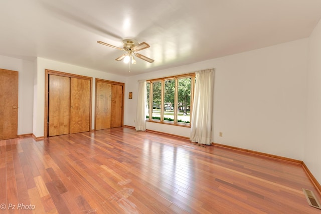 unfurnished bedroom with baseboards, visible vents, ceiling fan, light wood-type flooring, and two closets