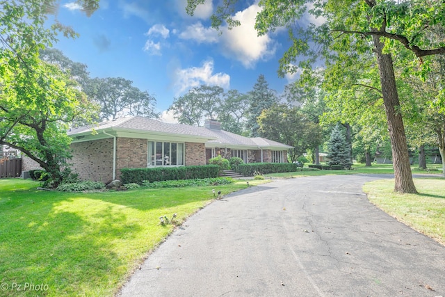 ranch-style house featuring brick siding, a chimney, a front yard, and aphalt driveway