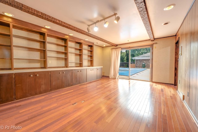 empty room with light wood finished floors, beamed ceiling, and rail lighting