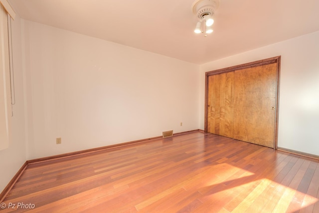 unfurnished bedroom featuring a closet, wood finished floors, visible vents, and baseboards