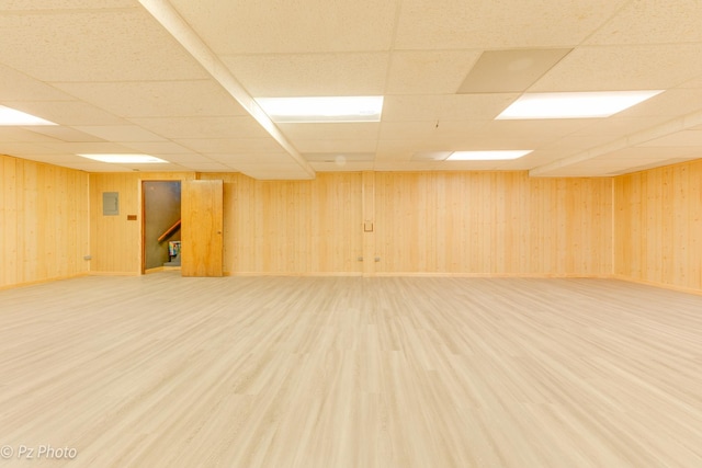 unfurnished room featuring baseboards, wood walls, a drop ceiling, and light wood-style floors