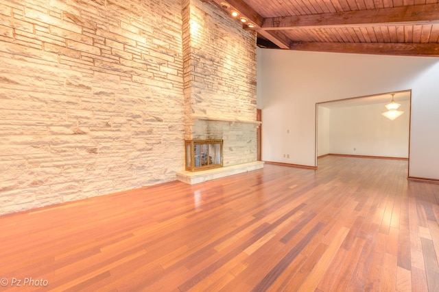 unfurnished living room with baseboards, wooden ceiling, wood finished floors, a stone fireplace, and beam ceiling