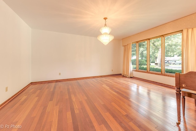 spare room featuring wood-type flooring, baseboards, and an inviting chandelier