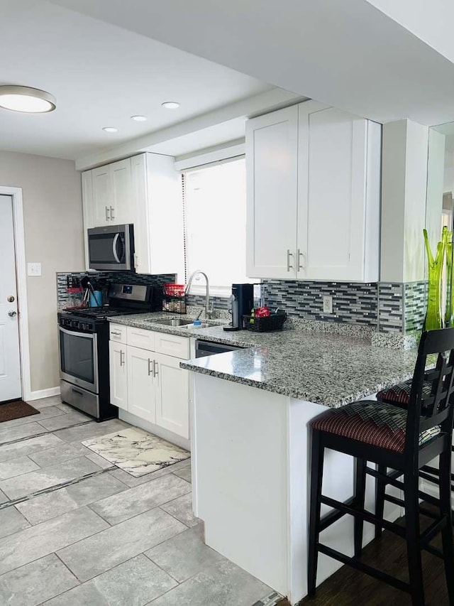 kitchen with appliances with stainless steel finishes, white cabinetry, sink, kitchen peninsula, and light stone countertops