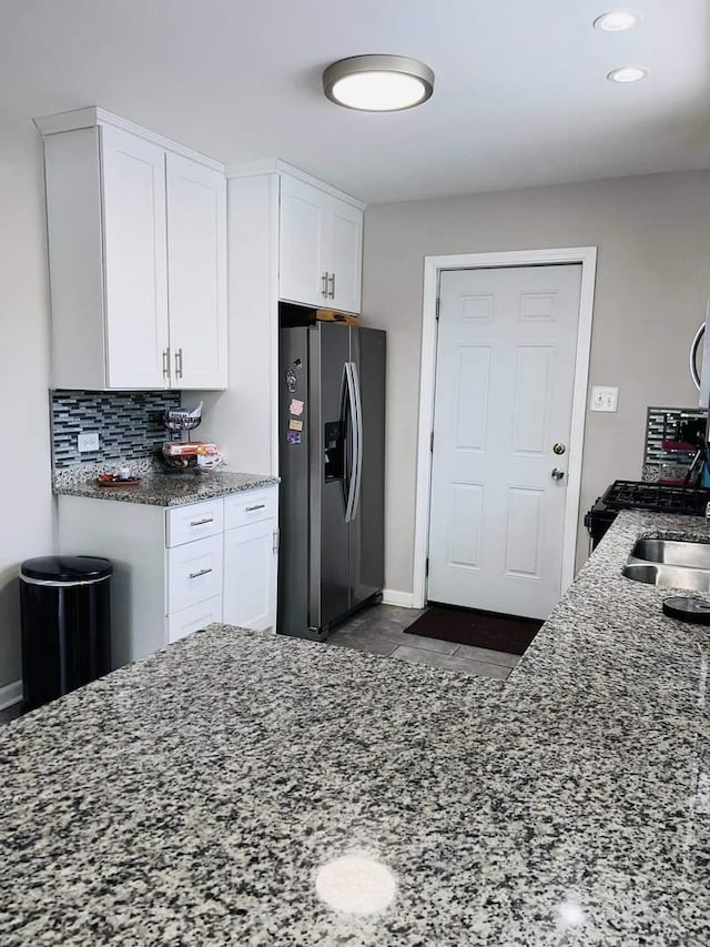 kitchen featuring white cabinetry, decorative backsplash, stainless steel fridge, and dark stone counters