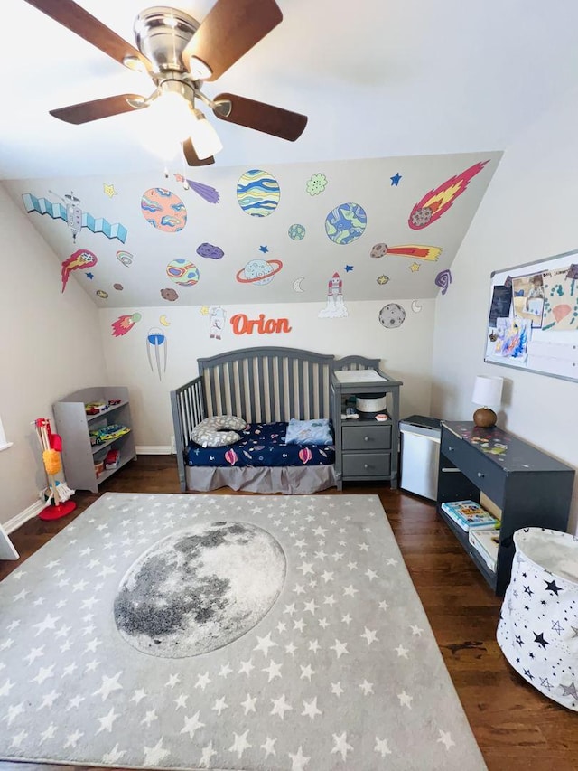 bedroom featuring a crib, dark hardwood / wood-style floors, ceiling fan, and vaulted ceiling