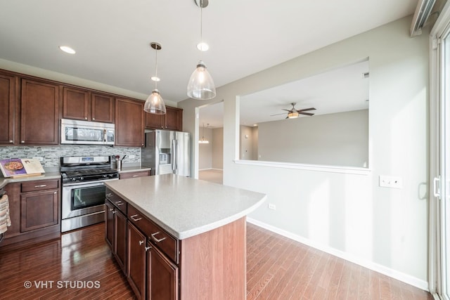 kitchen featuring hardwood / wood-style floors, stainless steel appliances, a center island, tasteful backsplash, and decorative light fixtures