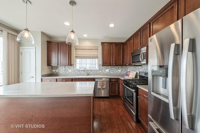 kitchen featuring appliances with stainless steel finishes, sink, backsplash, dark hardwood / wood-style flooring, and hanging light fixtures