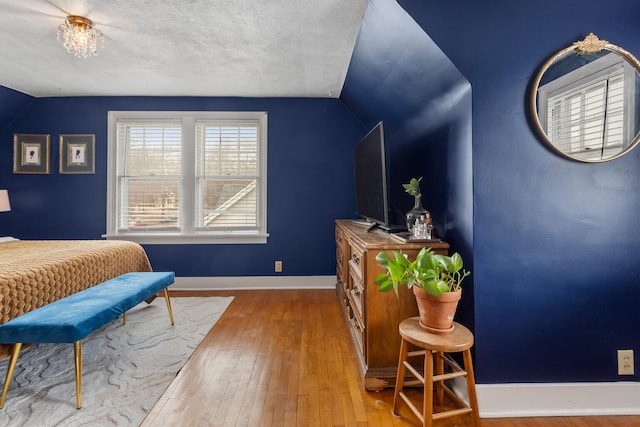 bedroom with vaulted ceiling, light hardwood / wood-style floors, and a textured ceiling