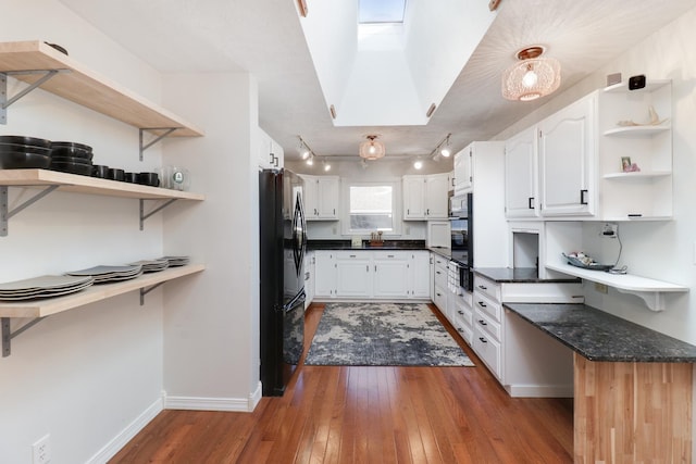 kitchen with white cabinets, dark hardwood / wood-style flooring, a skylight, and black appliances